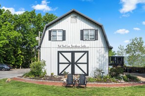 Un bâtiment blanc avec une grande porte de grange et deux fenêtres dotées de volets, portant l’inscription « Red Bud Cove Barnhouse Suites ».