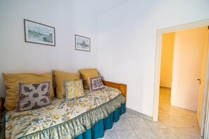 Un dormitorio con cama, dos almohadas y una colcha estampada con motivos florales. Hay dos cuadros en la pared.