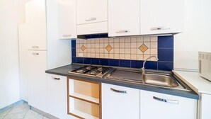 Een kleine keuken met witte kasten, een zwart aanrecht en een betegelde spatwand.