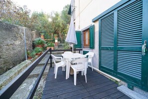 A patio with white plastic chairs and a table, a green shuttered door, and a stone wall. - Bilocale Marzia (Campo nell'Elba)
