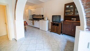 Een kleine keuken met witte kasten, een magnetron en een televisie op een houten standaard.