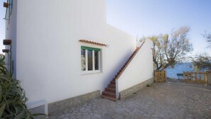 A white building with a stone-paved courtyard, a wooden staircase, and a small window with a green frame. - Villa Casa Bianca (Campo nell'Elba)