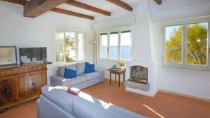 A living room with a fireplace, a sofa, a television, and a view of the sea. - Villa Casa Bianca (Campo nell'Elba)