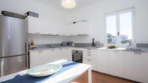 A modern kitchen with white cabinets, stainless steel appliances, and a window providing a view of the outside. - Villa Casa Bianca (Campo nell'Elba)