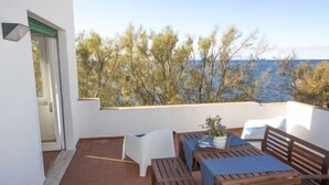 A balcony with a wooden table and chairs, a white chair, and a view of the sea and trees. - Villa Casa Bianca (Campo nell'Elba)
