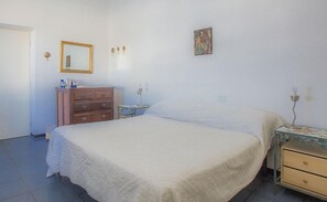 A bedroom with a bed, dresser, nightstand, lamp, and a painting on the wall.