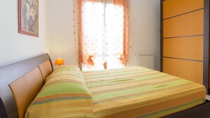 A bedroom with a bed, a nightstand, a lamp, a window with curtains, and a radiator. - Giulia (Campo nell'Elba)