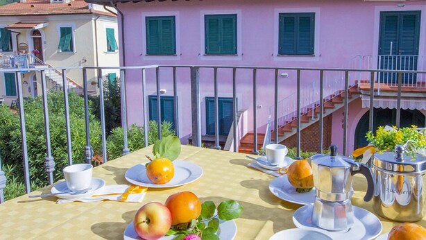 A table set with fruits, a cup, and a jug on a balcony with a view of a pink building.