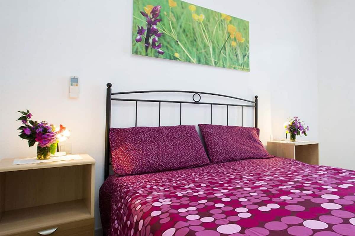 Une chambre à coucher avec un lit, deux tables de chevet, un tableau accroché au mur et une fenêtre.