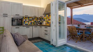 A compact kitchen with white cabinets, a colorful backsplash, and a dining area with a table and chairs. - App.ti Scaglieri Mare 1° piano (Portoferraio)