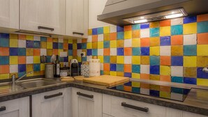 A kitchen with white cabinets, a stainless steel sink, and a colorful tiled backsplash. - App.ti Scaglieri Mare 1° piano (Portoferraio)