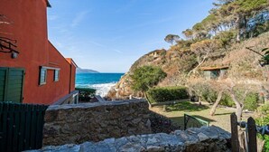 A coastal property with a stone wall, a red building, and a view of the sea. - App.ti Scaglieri Mare 1° piano (Portoferraio)