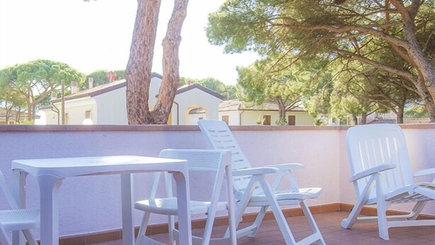A terrace with white plastic chairs and a table, surrounded by a low wall and trees. - Mansarda il Sarago (Campo nell'Elba)