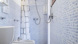 A bathroom with a white sink, a toilet, and a shower area with a tiled wall and floor. - Mansarda il Sarago (Campo nell'Elba)