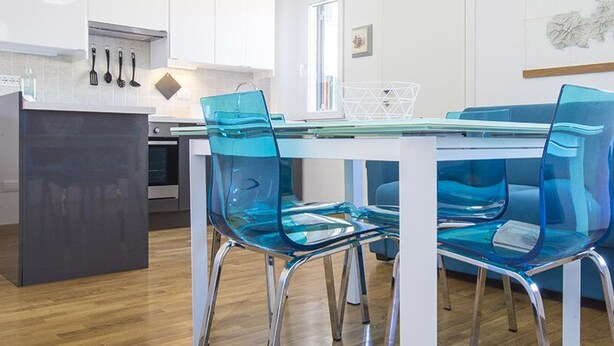 Una cocina moderna con armarios blancos, una mesa de comedor de vidrio y sillas azules.