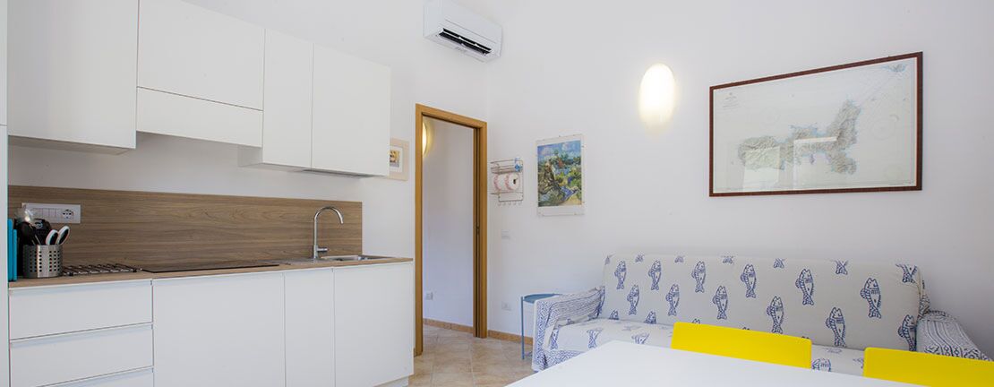 Eine moderne Küche mit weißen Schränken, einer Holz Arbeitsplatte und einem Spülbecken. Es gibt ein Sofa mit einem gemusterten Bezug und ein gerahmtes Bild an der Wand.