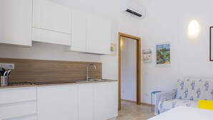 A modern kitchen with white cabinets, a wooden countertop, and a sink. There is a sofa with a patterned cover and a framed picture on the wall. - Punta dei Barbari (Rio)