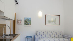 A small kitchenette with a sink and stove, a sofa with patterned cushions, and two framed pictures on the wall. - Punta dei Barbari (Rio)
