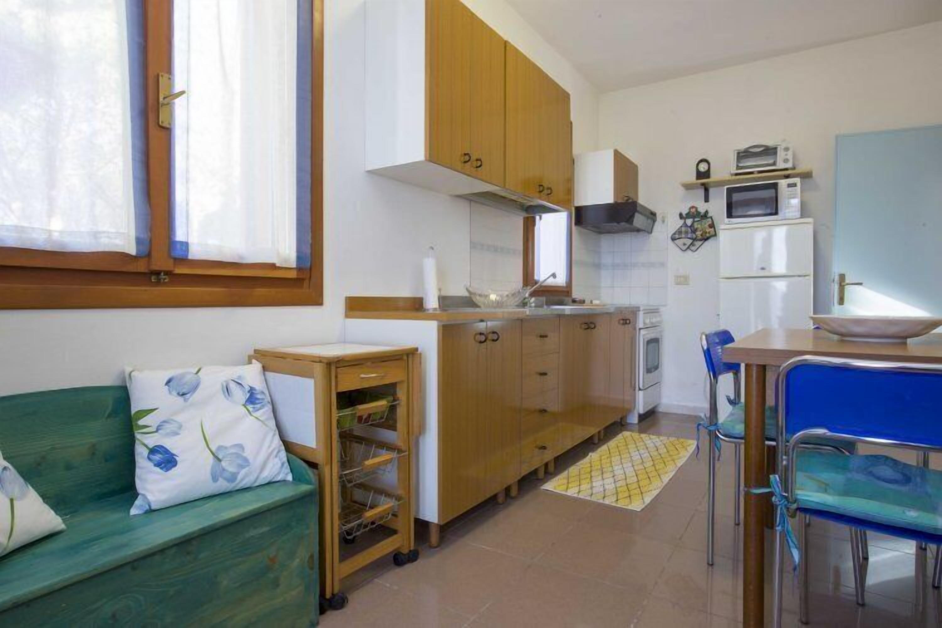A compact kitchen with wooden cabinets, a microwave, and a small refrigerator.