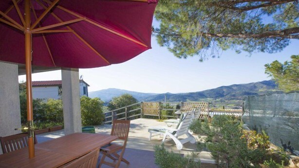 A patio with a wooden table and chairs, a red umbrella, and a view of mountains. - Santa Petronilla (Capoliveri)
