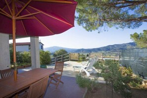 Un patio con una mesa y sillas de madera, una sombrilla roja y vistas a montañas.