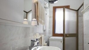 A bathroom with a white sink, a mirror, a towel rack, and a shower enclosure. - Santa Petronilla (Capoliveri)