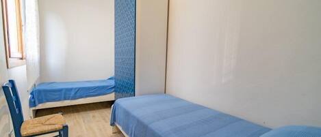 A small, single-room accommodation with two single beds, a chair, and a wardrobe.