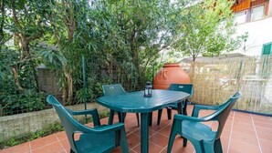 Eine Terrasse mit einem runden Tisch und vier Stühlen, umgeben von üppigem Grün und einem gefliesten Boden.