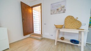 Ein Zimmer mit Holztür, weißer Wand mit gerahmtem Bild, einem gewebten Korb und einem kleinen Tisch mit Schalen.