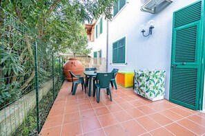 A patio with a tiled floor, a table with chairs, a large terracotta pot, and a wall with a window and a door. - Trilo Pozzo al Moro (Campo nell'Elba)