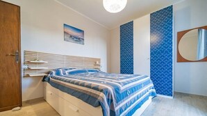 Ein Schlafzimmer mit einem Bett, einer Holztür, einem an der Wand befestigten Spiegel und einer blauen Wand mit Muster.