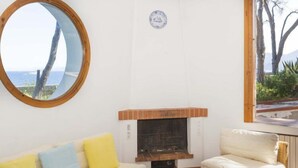 A cozy living room with a fireplace, a round mirror, and a view of the sea. - Villa Meridiana (Portoferraio)