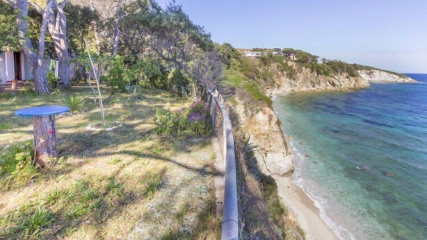 A coastal property with a grassy area, a blue table, and a paved path leading to the beach. - Villa Meridiana (Portoferraio)