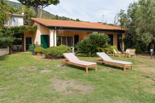 A two-story house with a tiled roof, a small balcony, and a garden with two sun loungers.