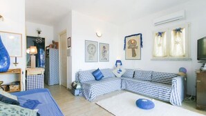 Un salon avec un canapé à rayures, un lit, une télévision et un mur décoré de tableaux encadrés et d’une croix.