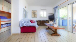Une chambre comprenant un lit, une petite table avec une chaise, un téléviseur et une porte-fenêtre coulissante donnant sur un espace extérieur.