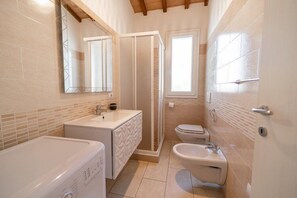 A compact bathroom with a shower, toilet, sink, and washing machine. - Villetta La Zanca (Marciana)
