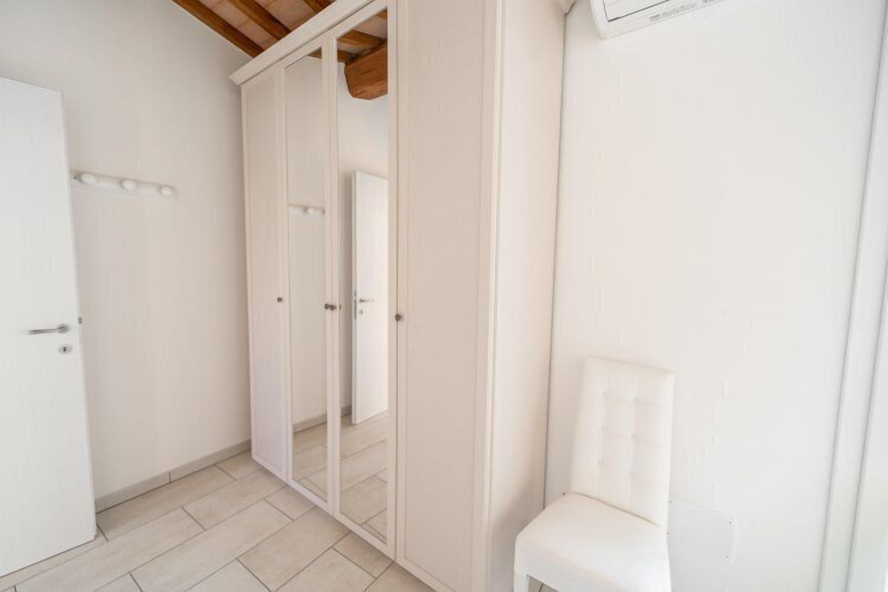 A room with a white wardrobe, a white chair, and a white door.