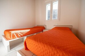 A room with two single beds, each with an orange bedspread, a window, and a white wall. - Villetta La Zanca (Marciana)