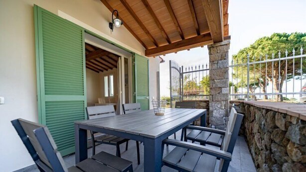 Eine Terrasse im Freien mit Tisch und Stühlen, einer Steinmauer und einem Metallgitter.