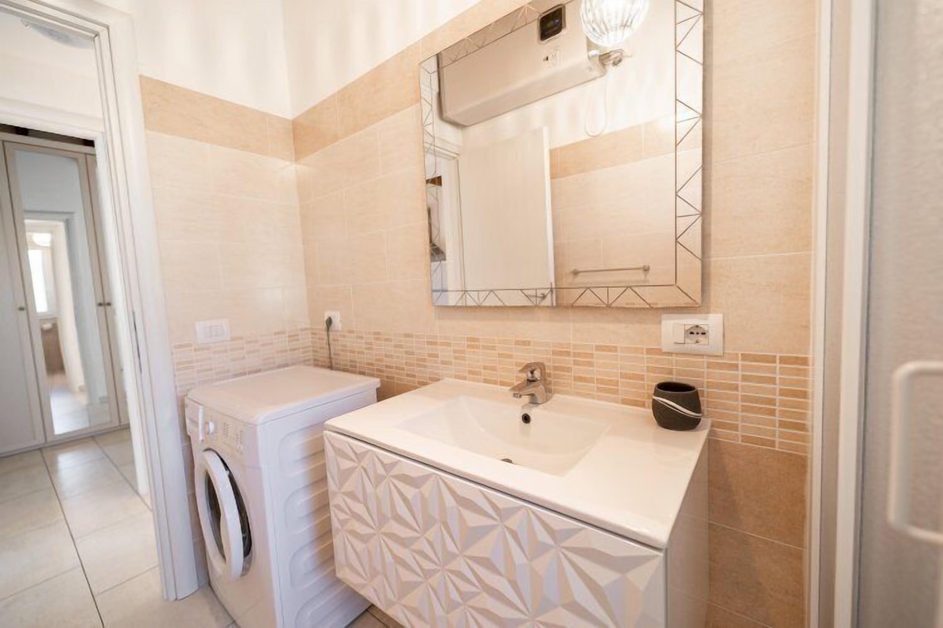A modern bathroom with a built-in washing machine, a large mirror, and a sink.