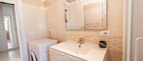 A modern bathroom with a built-in washing machine, a large mirror, and a sink.