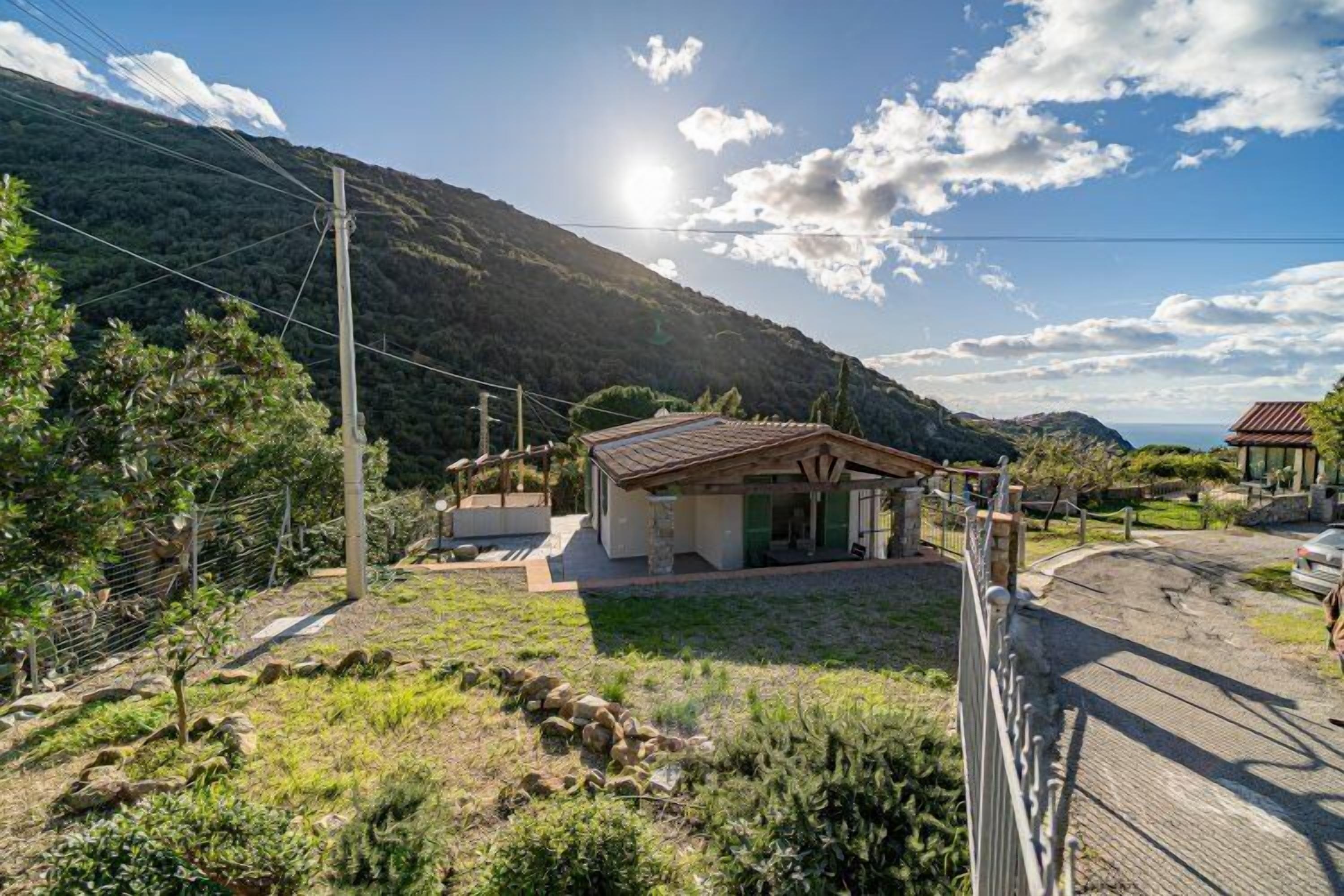 A house with a sloped roof, surrounded by a fenced yard, with a mountain in the background.