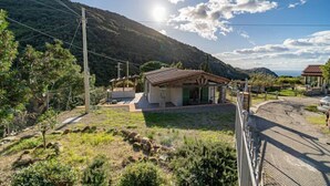 Ein Haus mit geneigtem Dach, umgeben von einem eingezäunten Garten, mit einem Berg im Hintergrund.