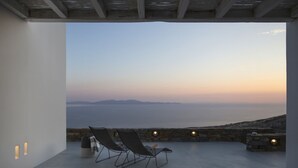 A balcony with two lounge chairs, a stone wall, and a view of the sea and distant mountains. - House G in Kardiani Tinos (Tinos)