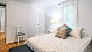 Un dormitorio con una cama, una silla, una mesita de noche, una lámpara y una puerta.