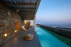 A stone-walled infinity pool with a hanging chair and a round seating area. - House Y in Kardiani Tinos (Tinos)
