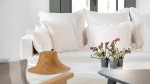 A white sofa with multiple pillows, a woven hat, and small potted plants on a table. - House Y in Kardiani Tinos (Tinos)