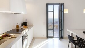 A modern kitchen with a large window, a dining area with a table and chairs, and a view of the landscape. - House Y in Kardiani Tinos (Tinos)