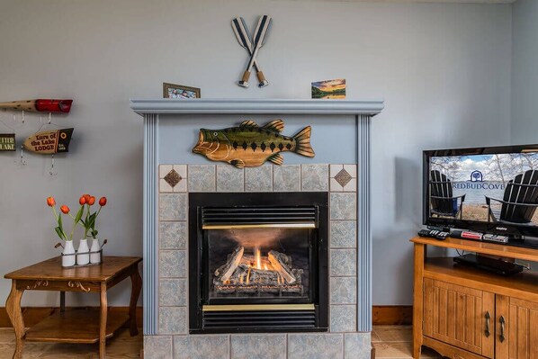 A fireplace with a fish decoration, a television, and a small table with vases.